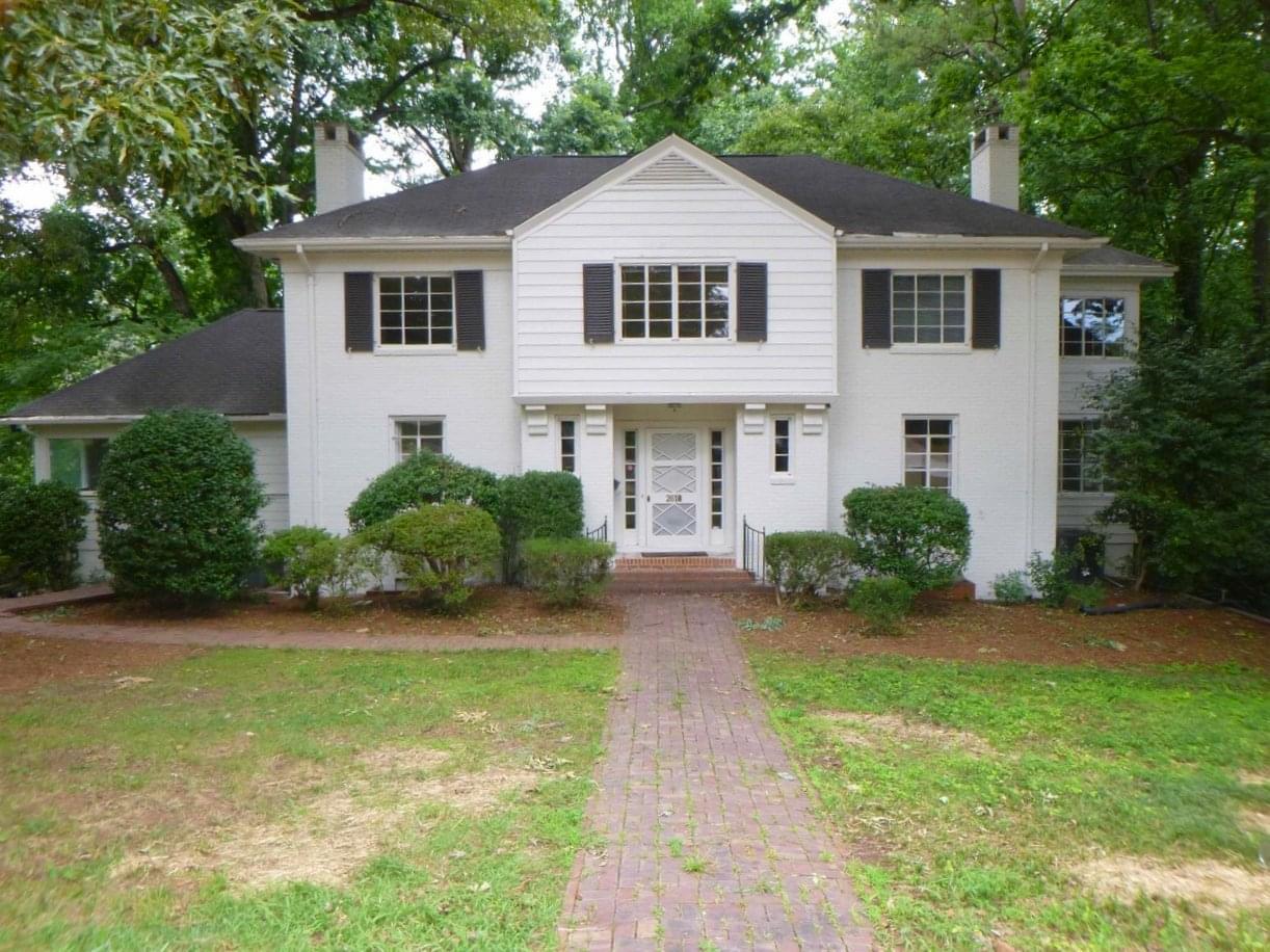 A two-story white home with dark shutters, a stone front path, symmetrical front entrance, green lawn, surrounded by trees